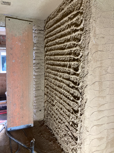 Lehmputz-Rohbau Strukturierter Lehmputz in horizontalen Rillen an der Wand, neben Holzrahmen – atmungsaktiv und texturiert.