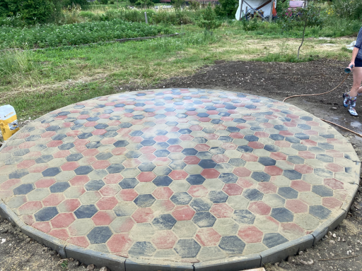 Hexagon-Terrasse Rundes hexagonales Pflaster aus rot-grau Beige Betonziegeln auf frischem Gartengrund – modern und robust.